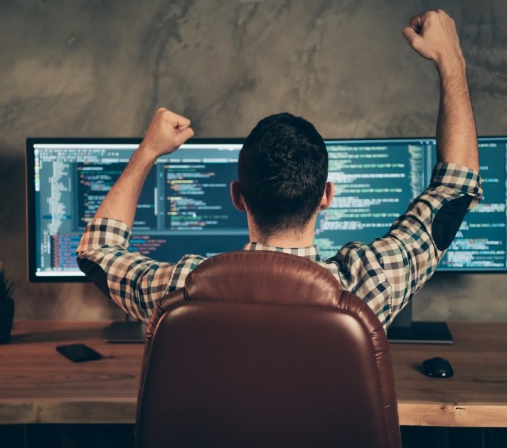 Tevreden ontwikkelaar achter twee schermen met code